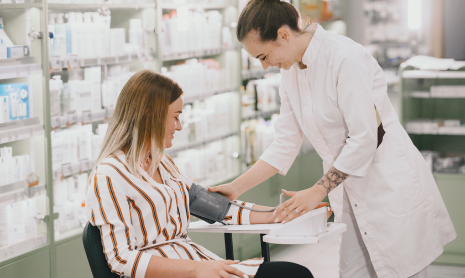 Mitarbeiterin misst den Blutdruck einer Kundin in einer Apotheke